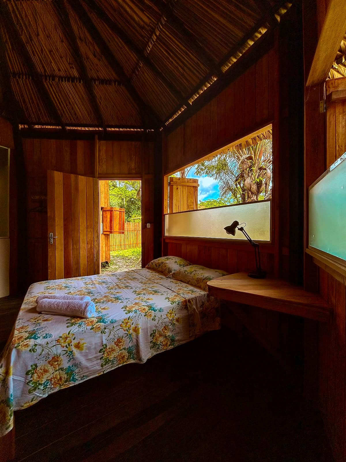 Cama de casal com porta aberta para o jardim e vista da janela para o mato