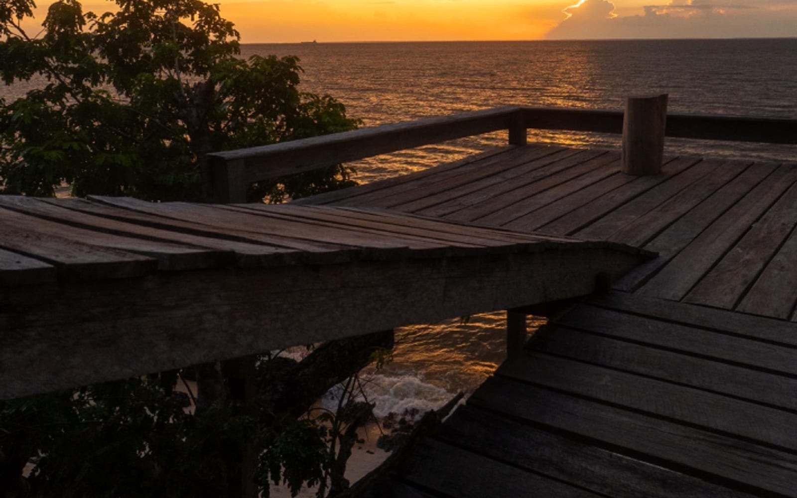 Deck de madeira da pousada avançando sobre o rio ao pôr do sol